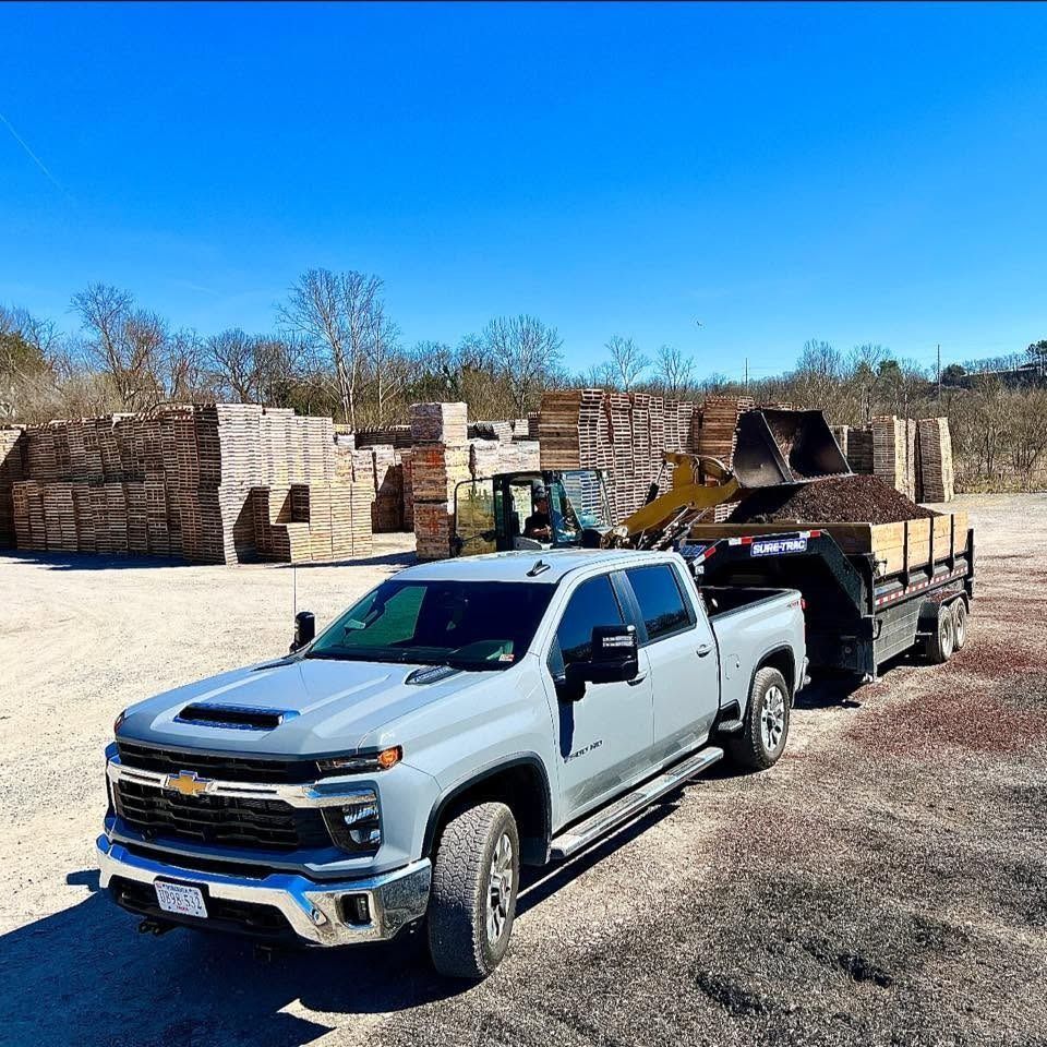 Silver pickup truck towing a trailer with stone blocks in a quarry yard under a clear blue sky