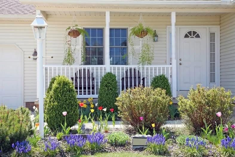 Front porch with white house, hanging plants, and a colorful flower garden in front