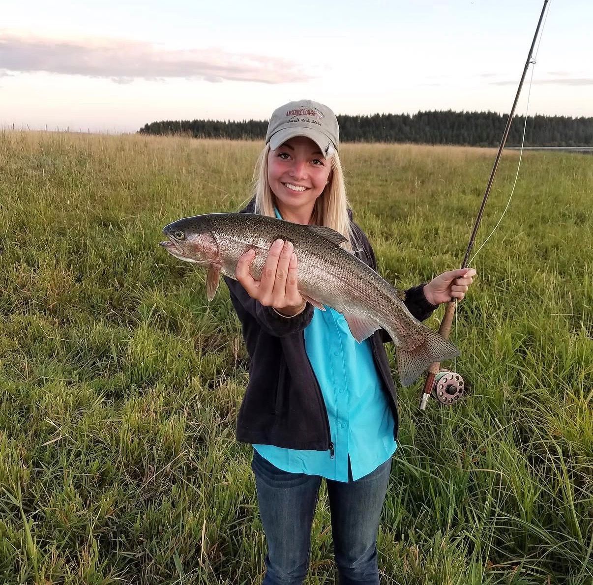 A person is holding a rainbow trout in their hands in the water.