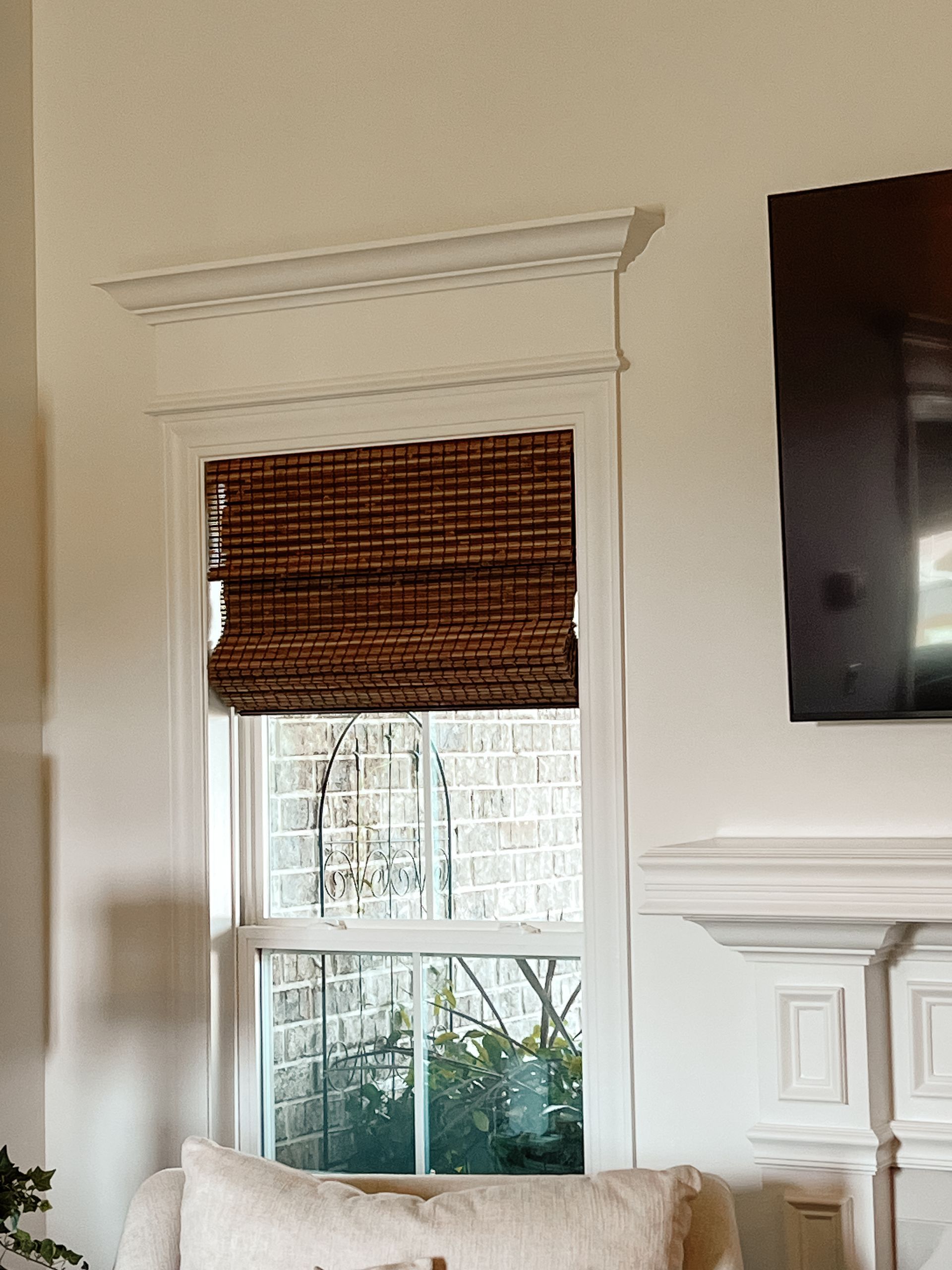 A living room with a couch a fireplace and a television with a natural woven shade on window.