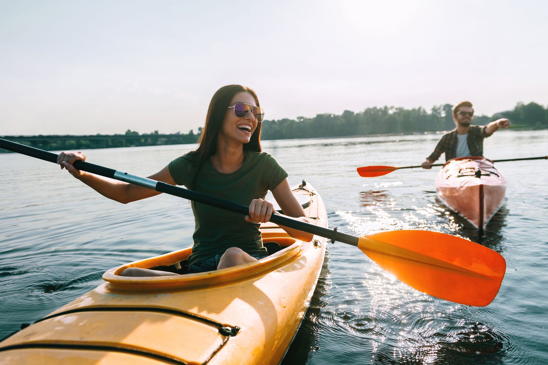 A man and a woman are paddling kayaks on a lake.