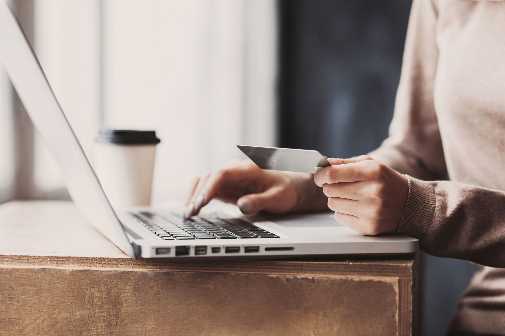 A woman is holding a credit card while using a laptop computer.