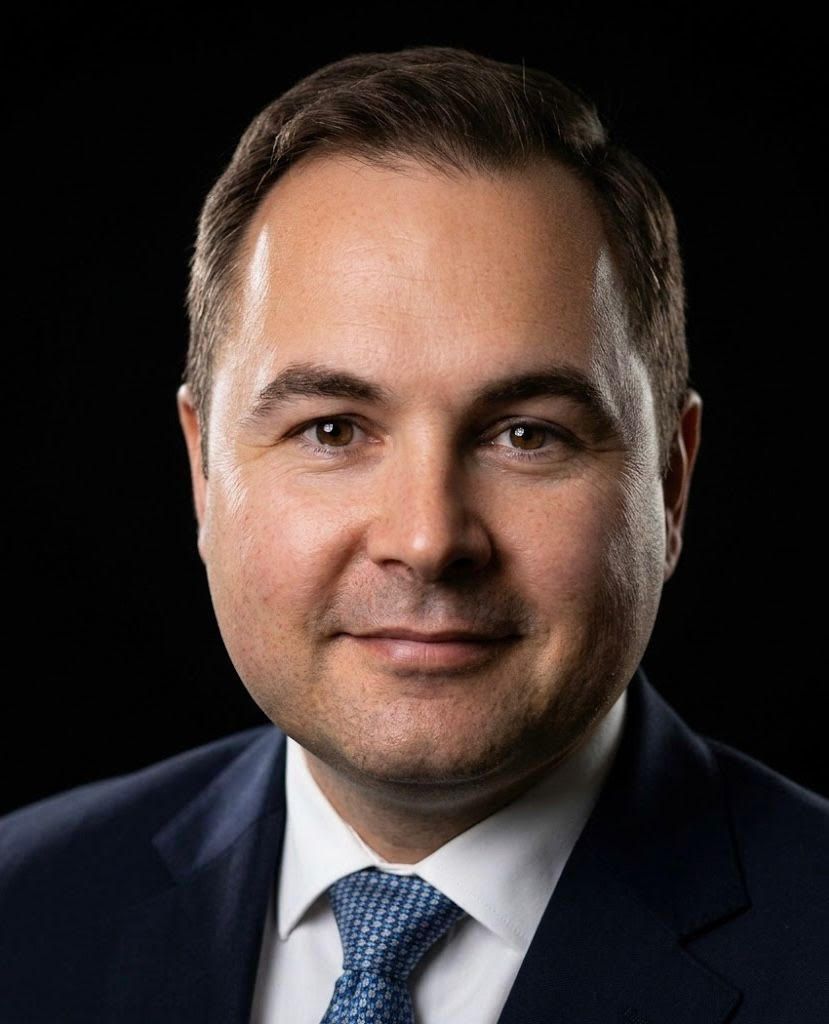 Studio headshot of a man in a dark suit and blue tie against a black background