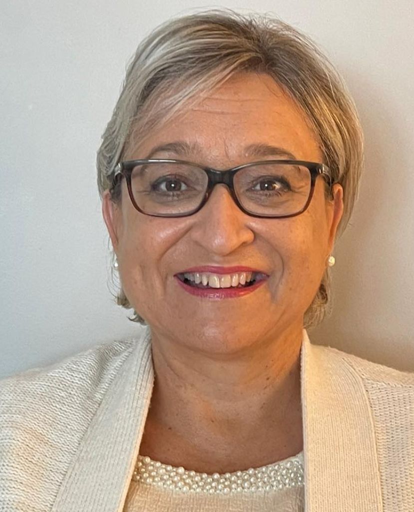 A woman wearing glasses and a white jacket is smiling for the camera.