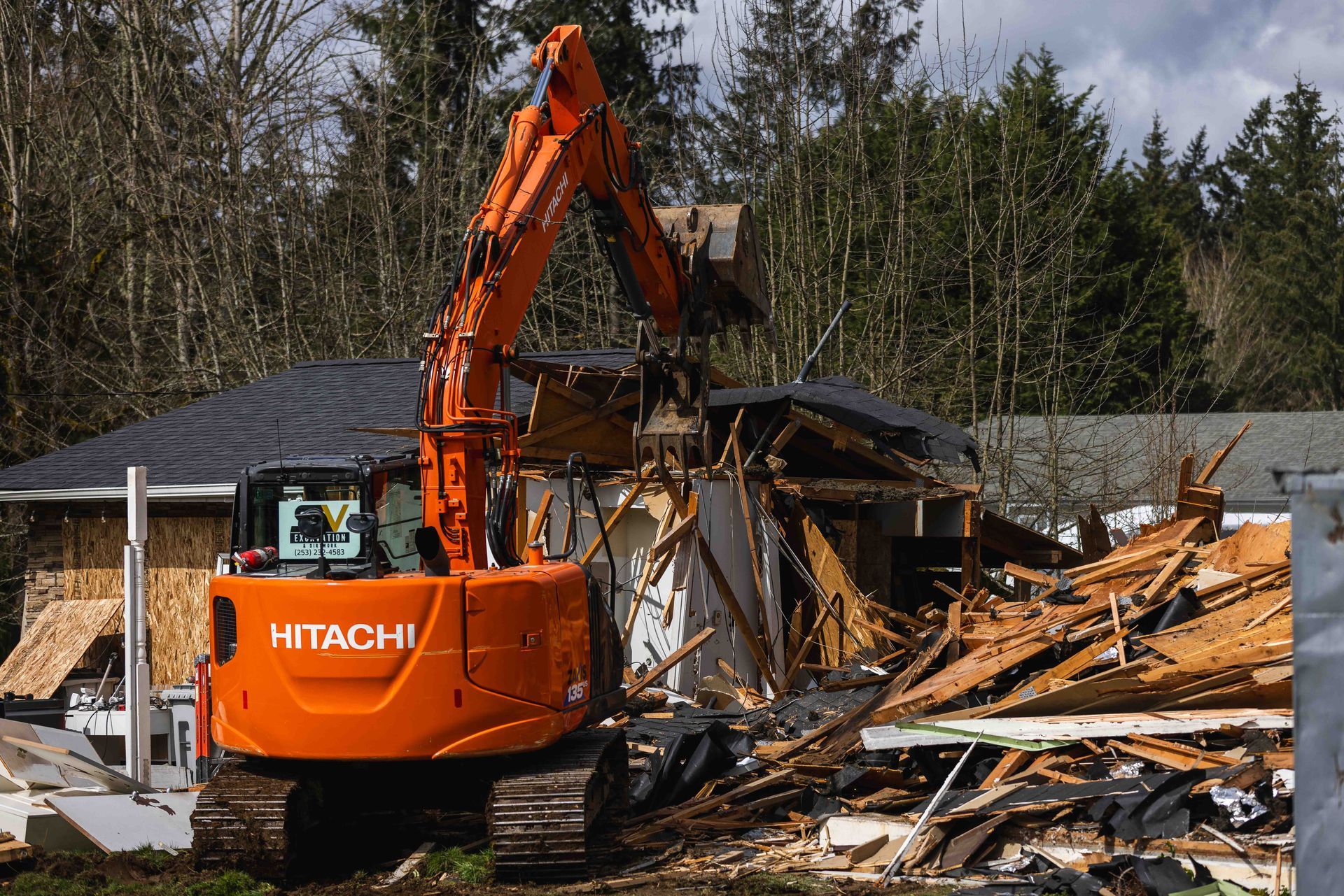 A large orange excavator is demolishing a house.