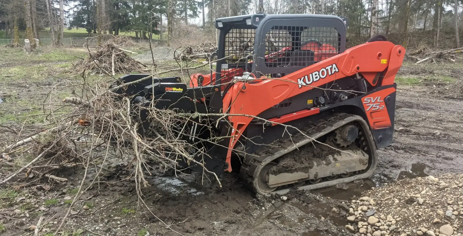 A red and black kubota skid steer is driving through a muddy field.