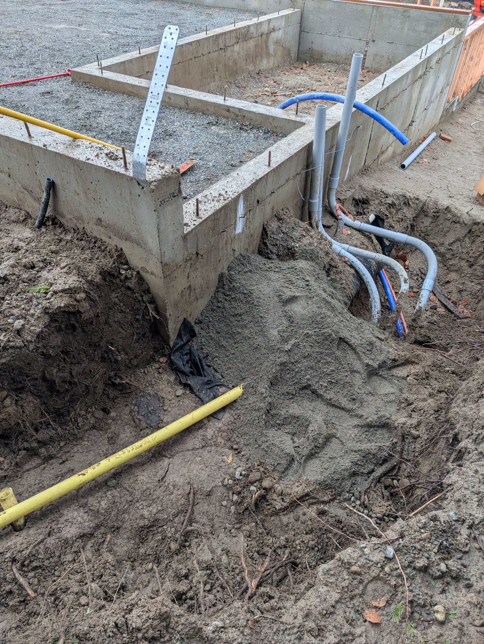 A bunch of pipes are laying in the dirt next to a concrete wall.