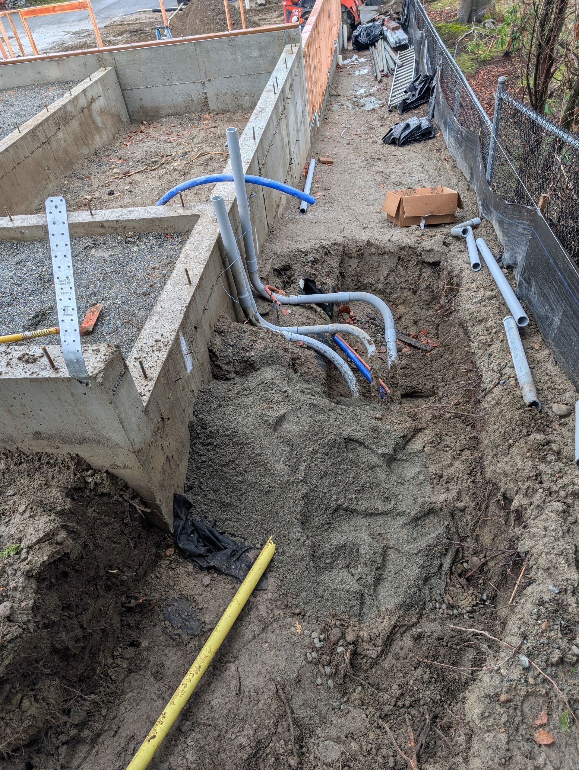 A bunch of pipes are laying in the dirt next to a concrete wall.