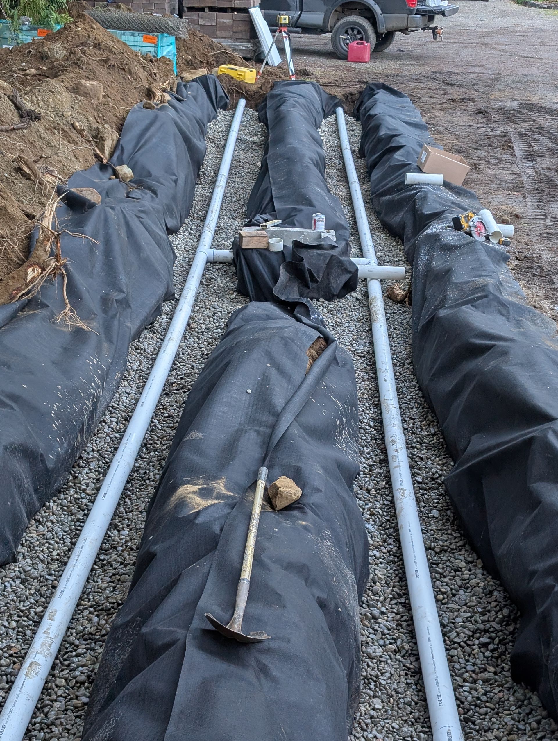 A row of pipes covered in black tarps are being installed in the dirt.