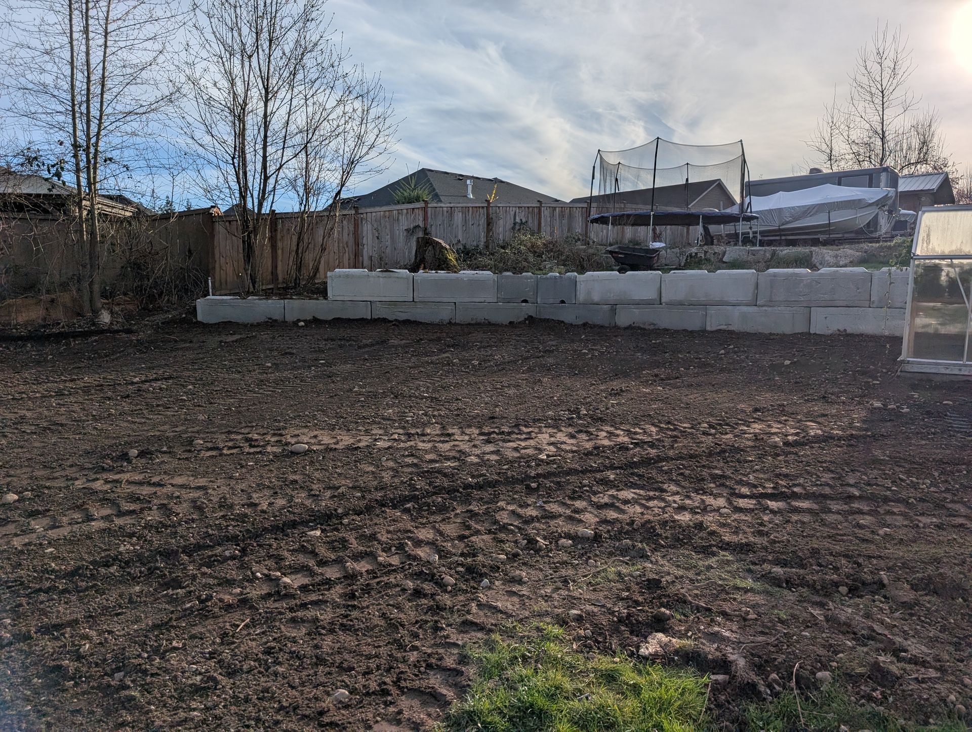 A dirt field with a fence and a greenhouse in the background.