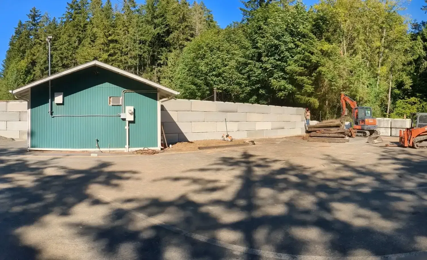 A green shed with a white roof is in a parking lot next to a concrete wall.
