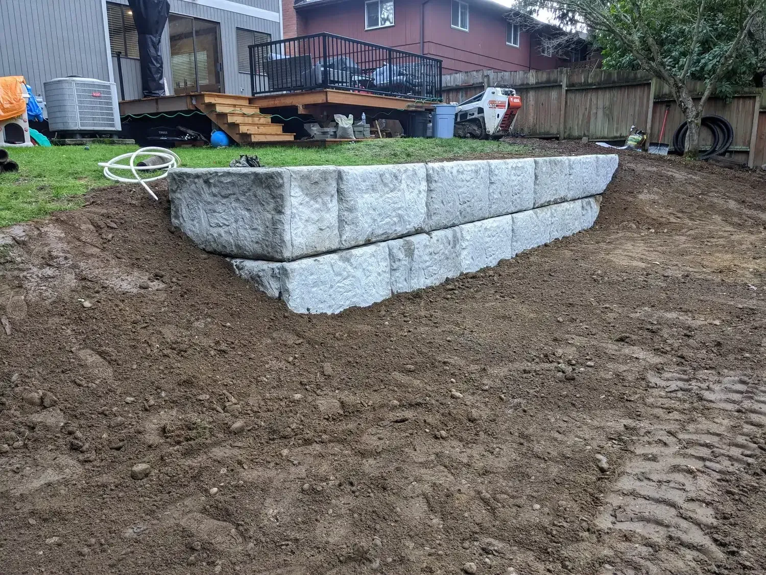 A concrete wall is being built in a backyard next to a house.