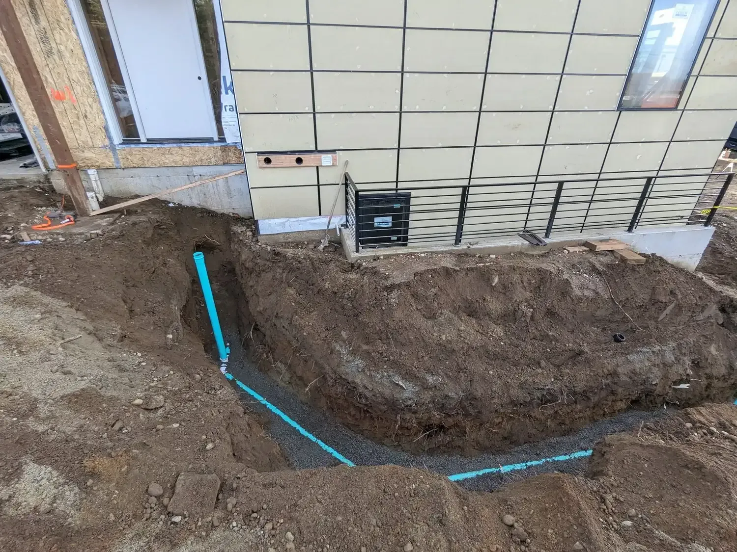 A drain pipe is being installed in the dirt in front of a building.
