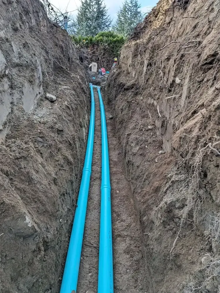 A blue pipe is being installed in a trench.