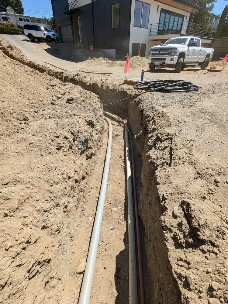 A white truck is parked in the dirt next to a pipe.