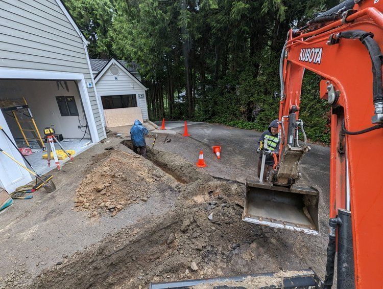 An excavator is digging a hole in the ground in front of a house.