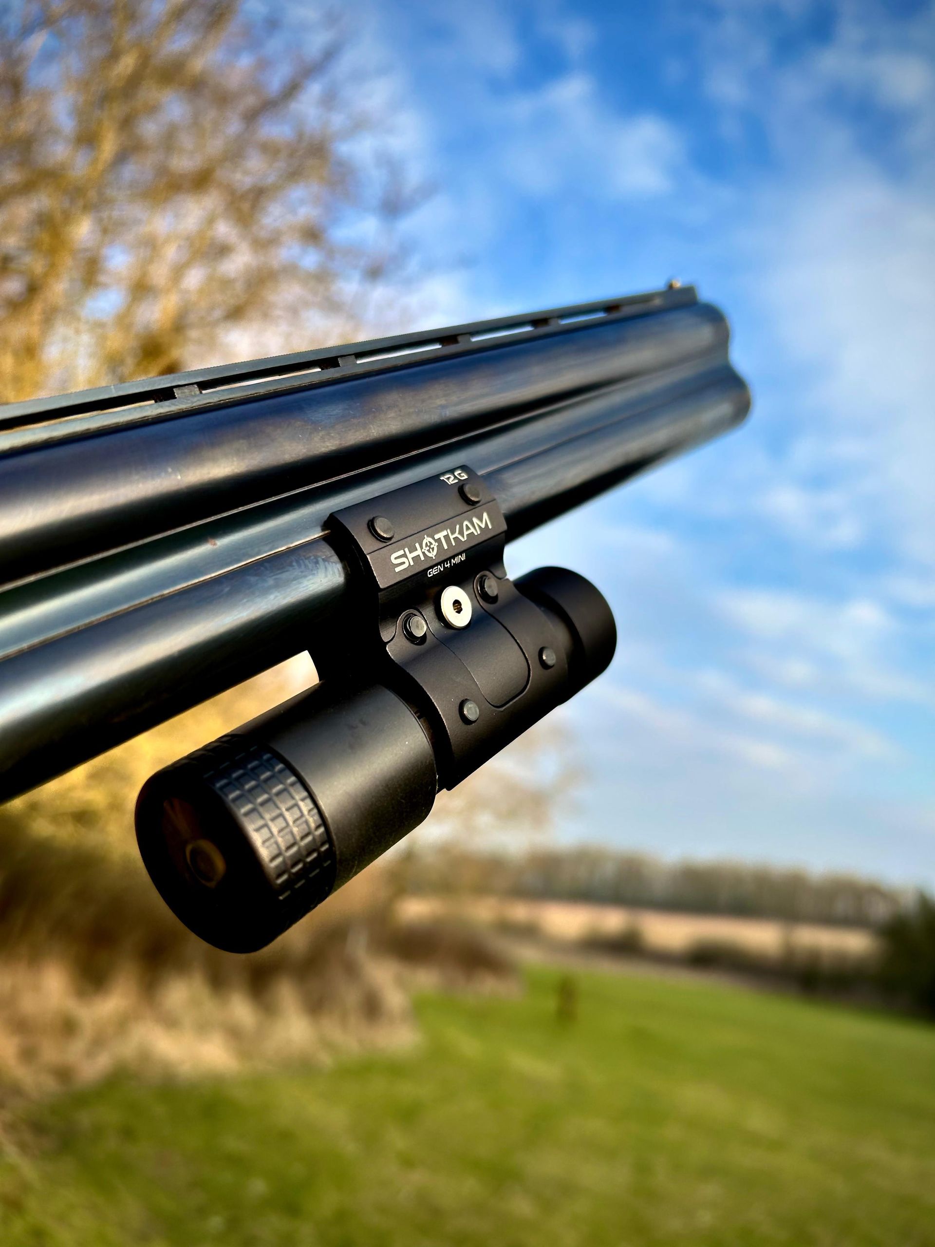 Close-up of a shotgun barrel with a mounted black light in a field with a blue sky.