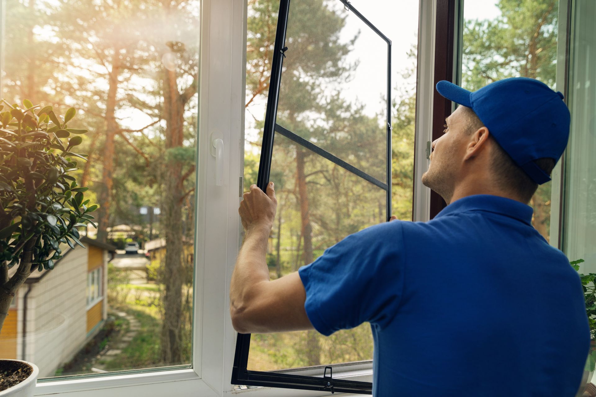 A man is installing a mosquito net on a window.