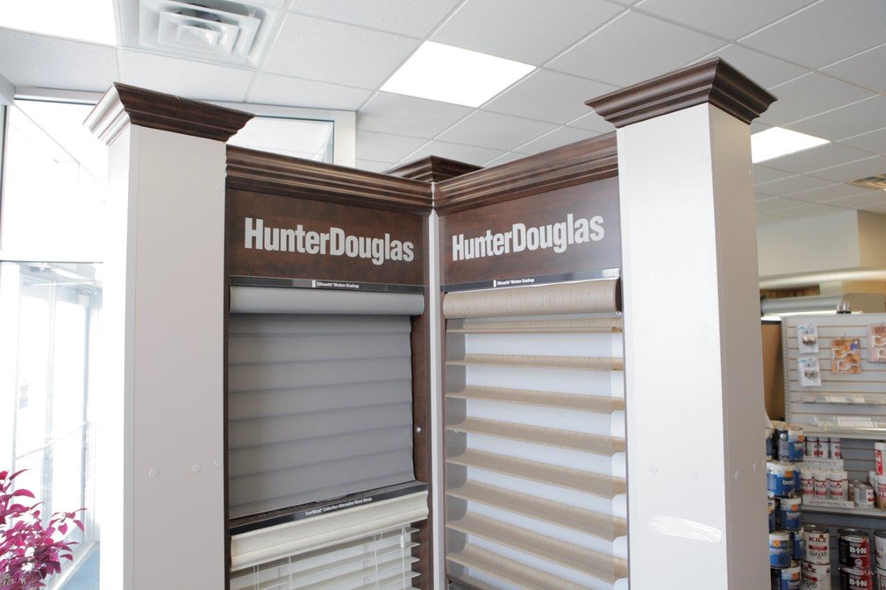 Hunter Douglas window shade displays in a showroom. Dark brown crown molding and white columns.