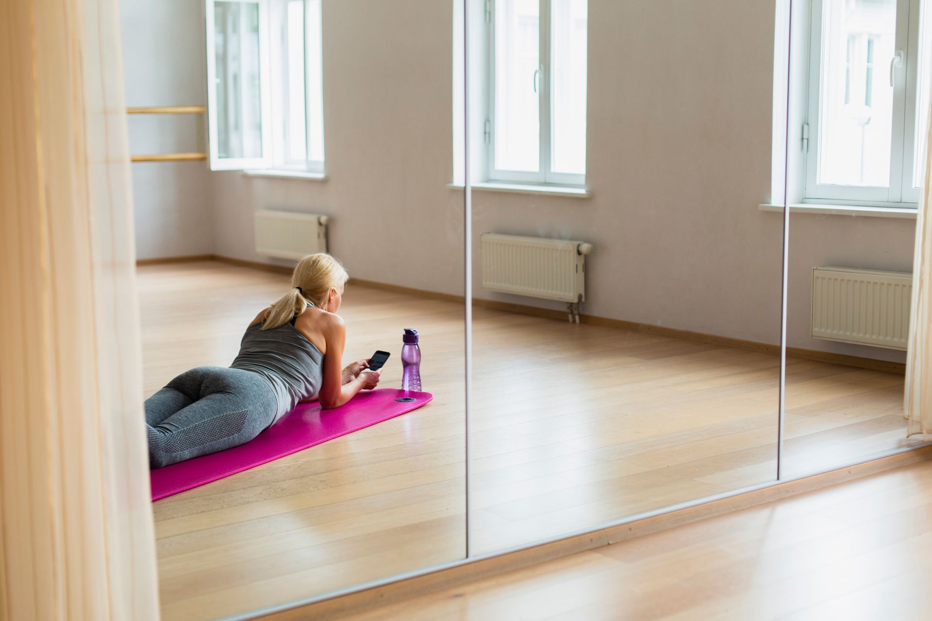 A woman is laying on a yoga mat in front of a large mirror.