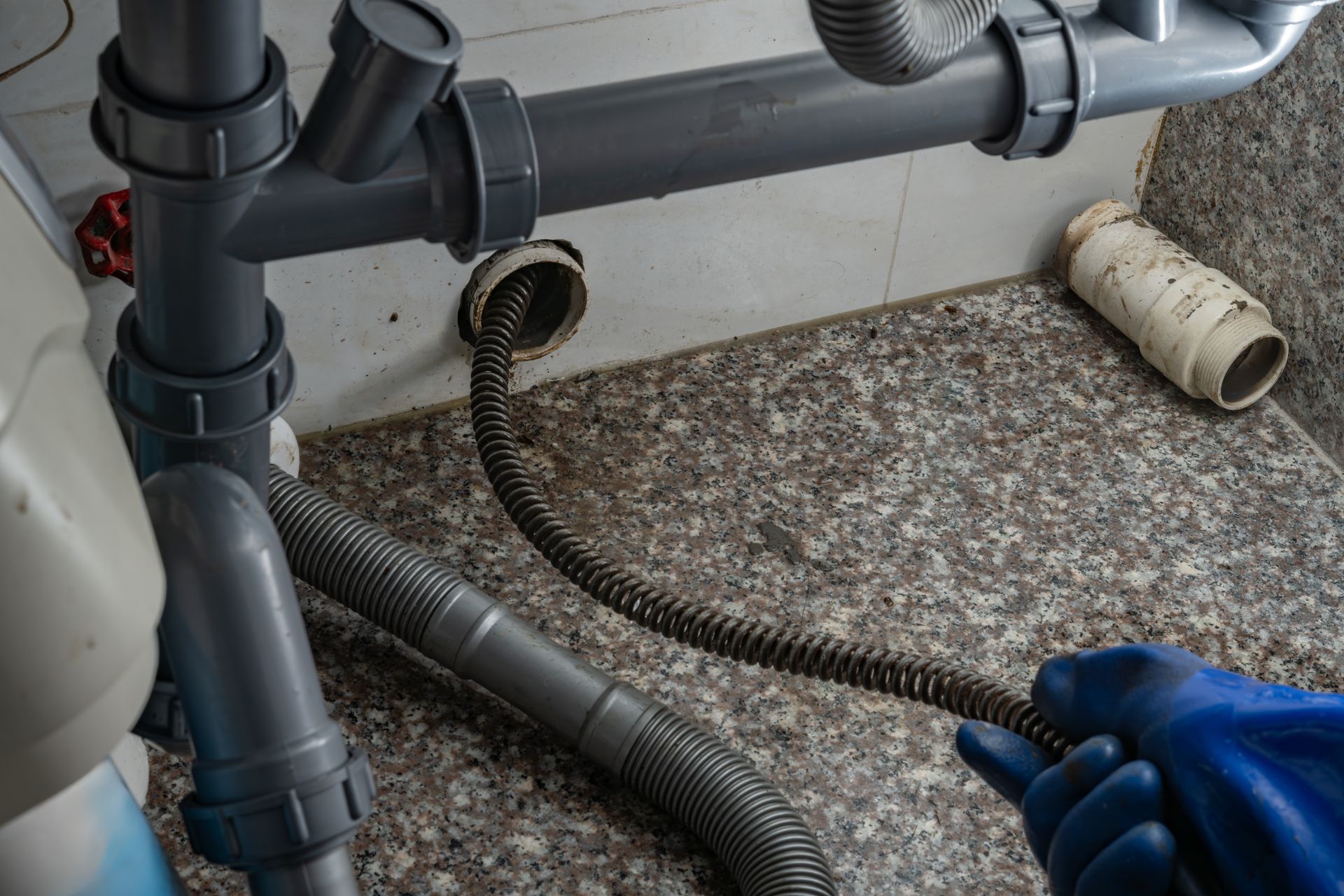 Metal drain snake inserted into under-sink piping during a commercial drain cleaning service.