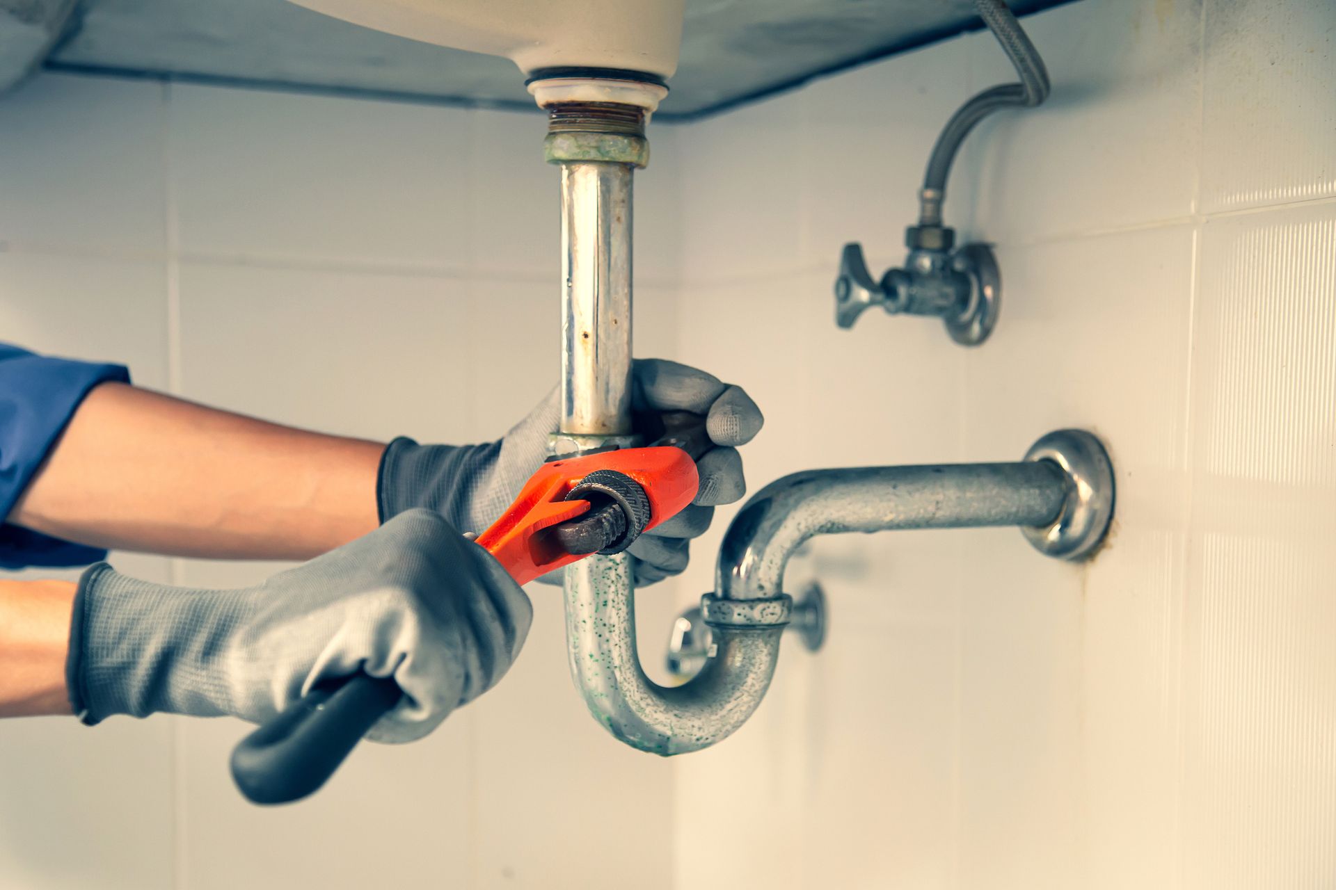 Plumber fixing under sink drain pipe with wrench during plumbing repair service to restore flow fast.
