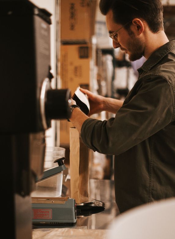 A man is using a machine to seal a bag of coffee.