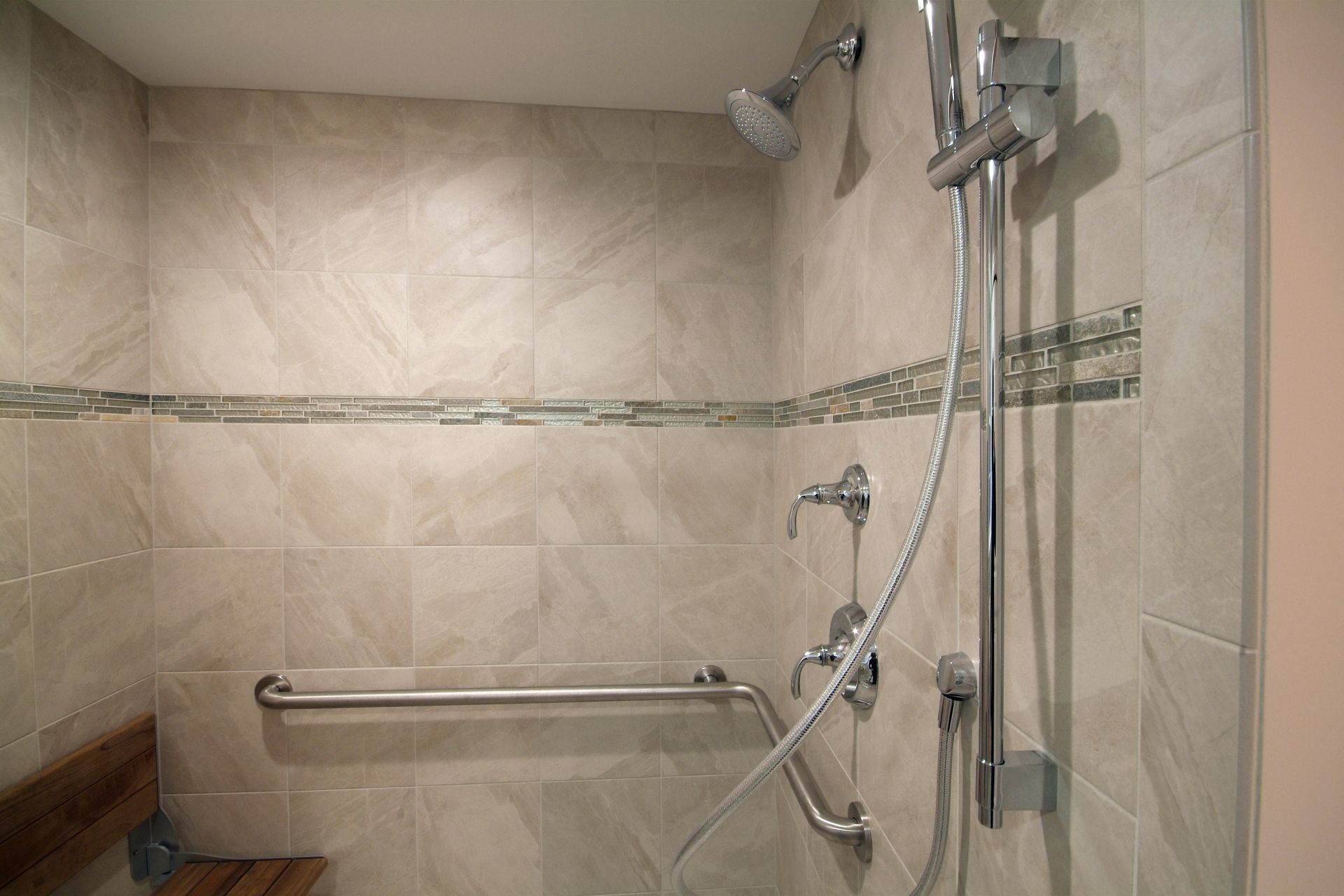 Walk-in shower with beige tile, grab bars, handheld showerhead, and built-in seat