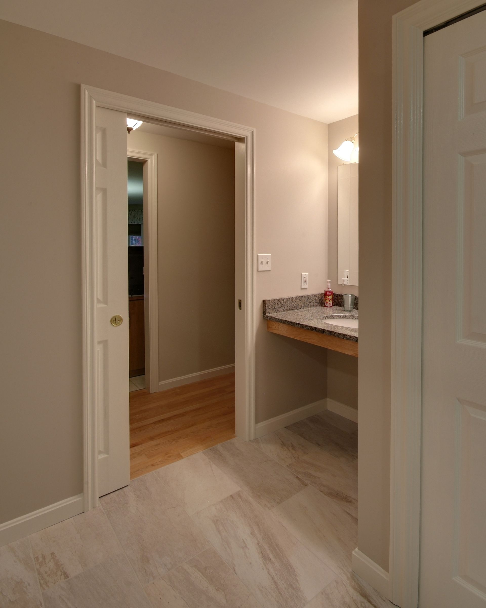 Small hallway with open doorways, light wood floors, and a granite countertop under a wall sconce.