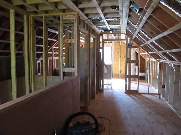 Unfinished house interior with exposed framing, sloped ceiling, and a bright doorway at the far end