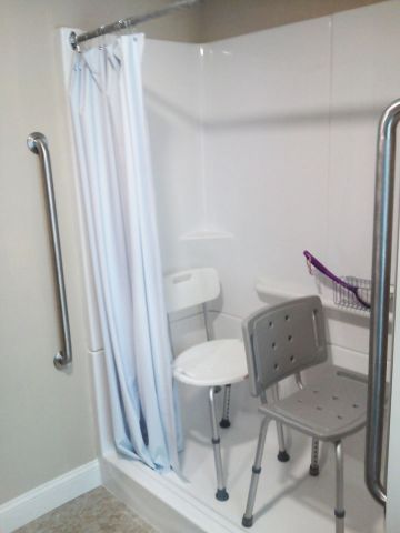 Accessible shower with chair, grab bars, and a white curtain in a bathroom.