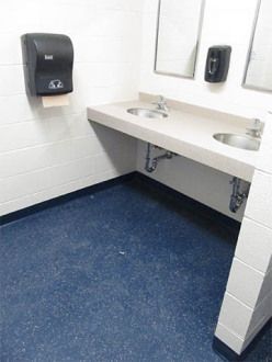 Empty public restroom with white sink, wall-mounted dispenser, and blue floor.