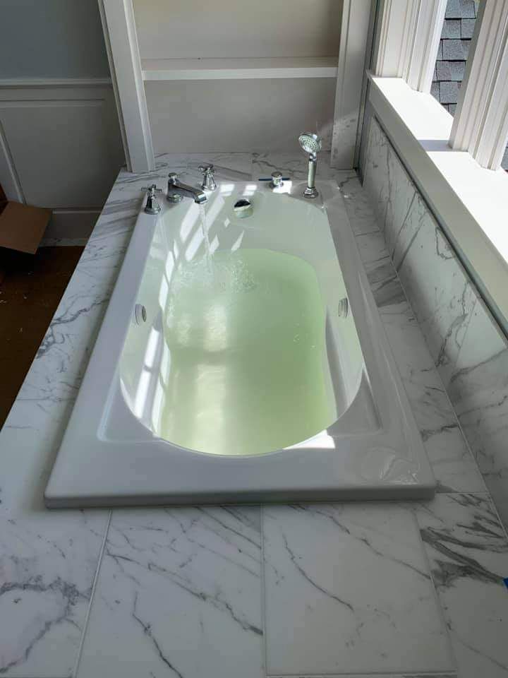 Bathtub filled with pale green water in a marble-tiled bathroom beside a window