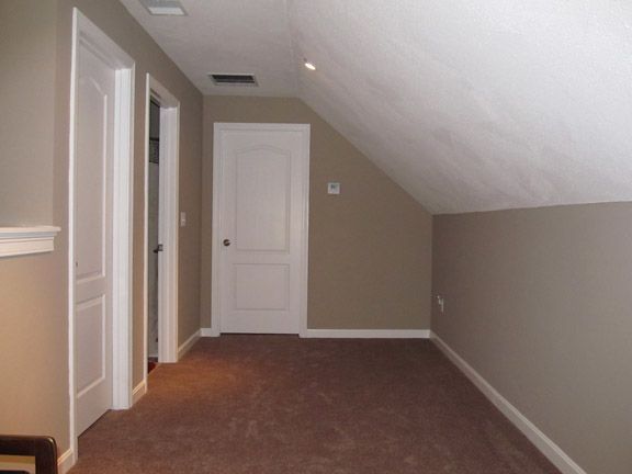 Empty carpeted attic hallway with beige walls, sloped white ceiling, and two white doors.