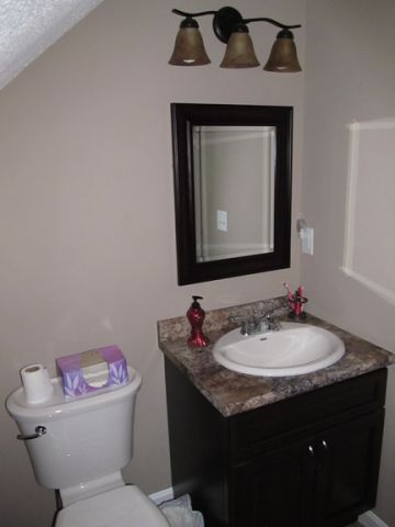 Small bathroom with a toilet, dark vanity and mirror, granite countertop, and three-light fixture above.