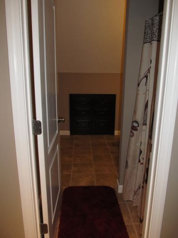 Narrow hallway with tile floor, open doors, and a dark cabinet at the far end