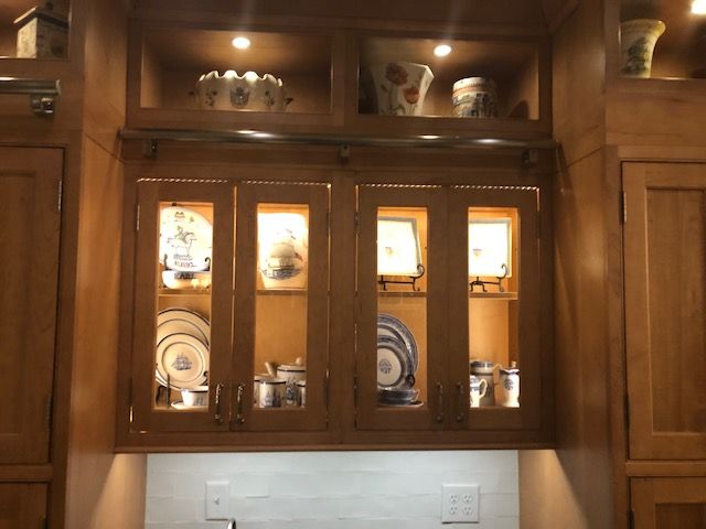 Wooden kitchen cabinets with glass-front doors and lit display shelves above a countertop