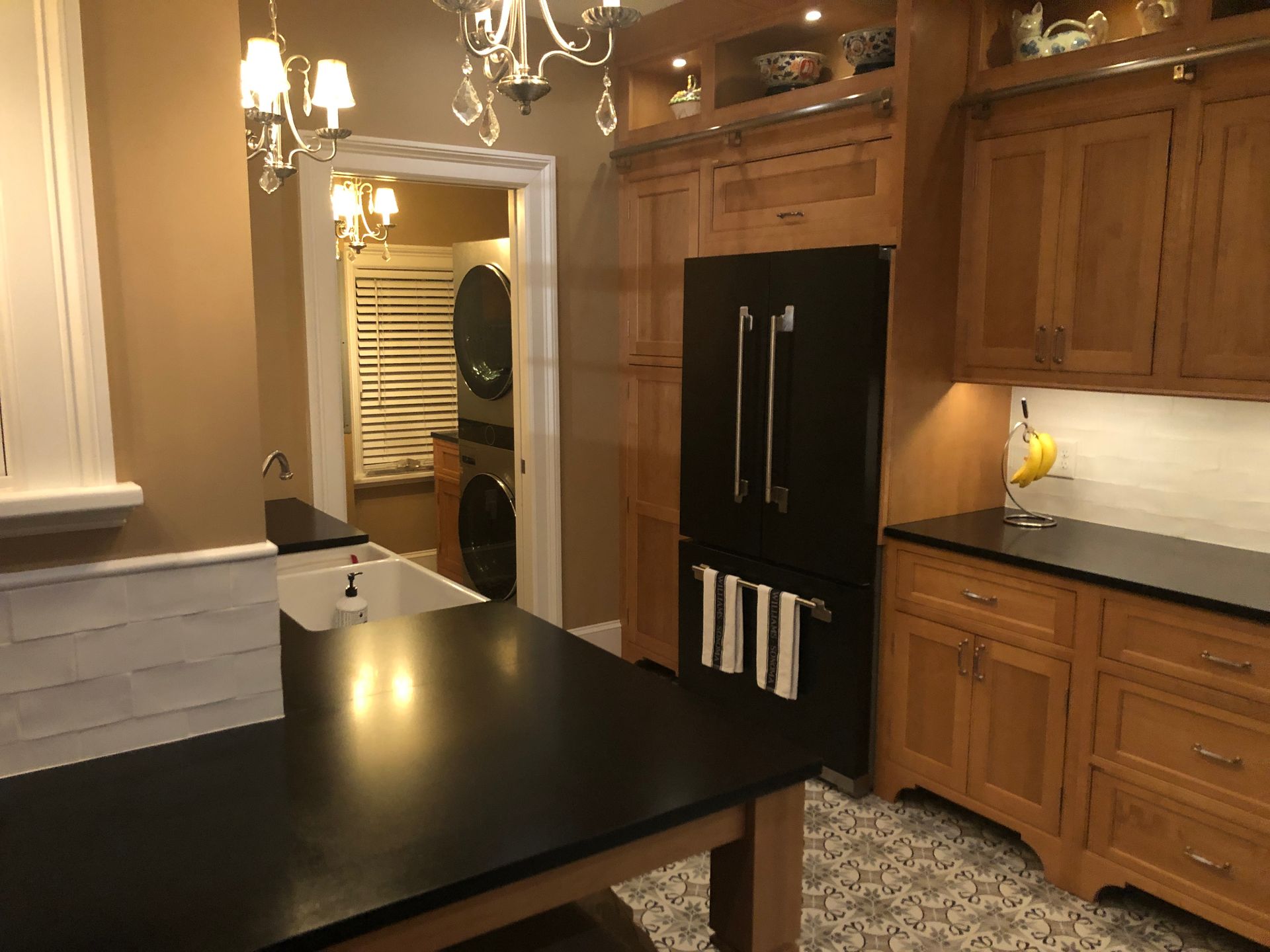 Kitchen with black island countertop, wood cabinets, stainless appliances, and warm lighting