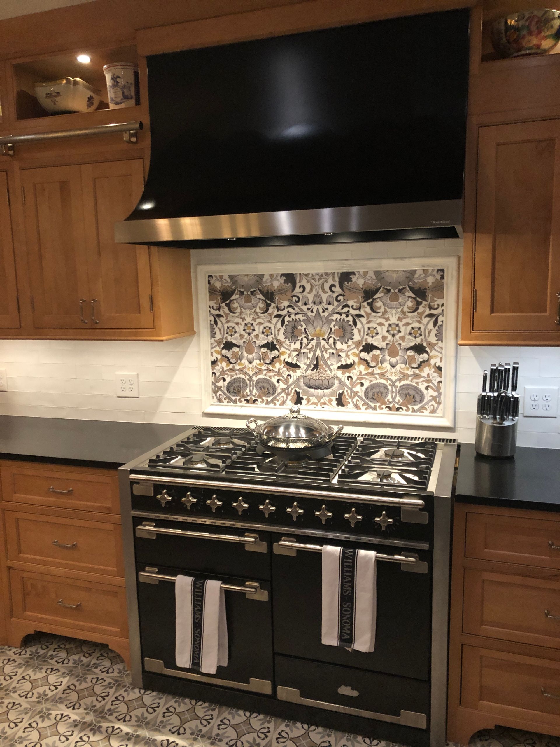 Kitchen with black range and hood, patterned tile backsplash, and wooden cabinets.