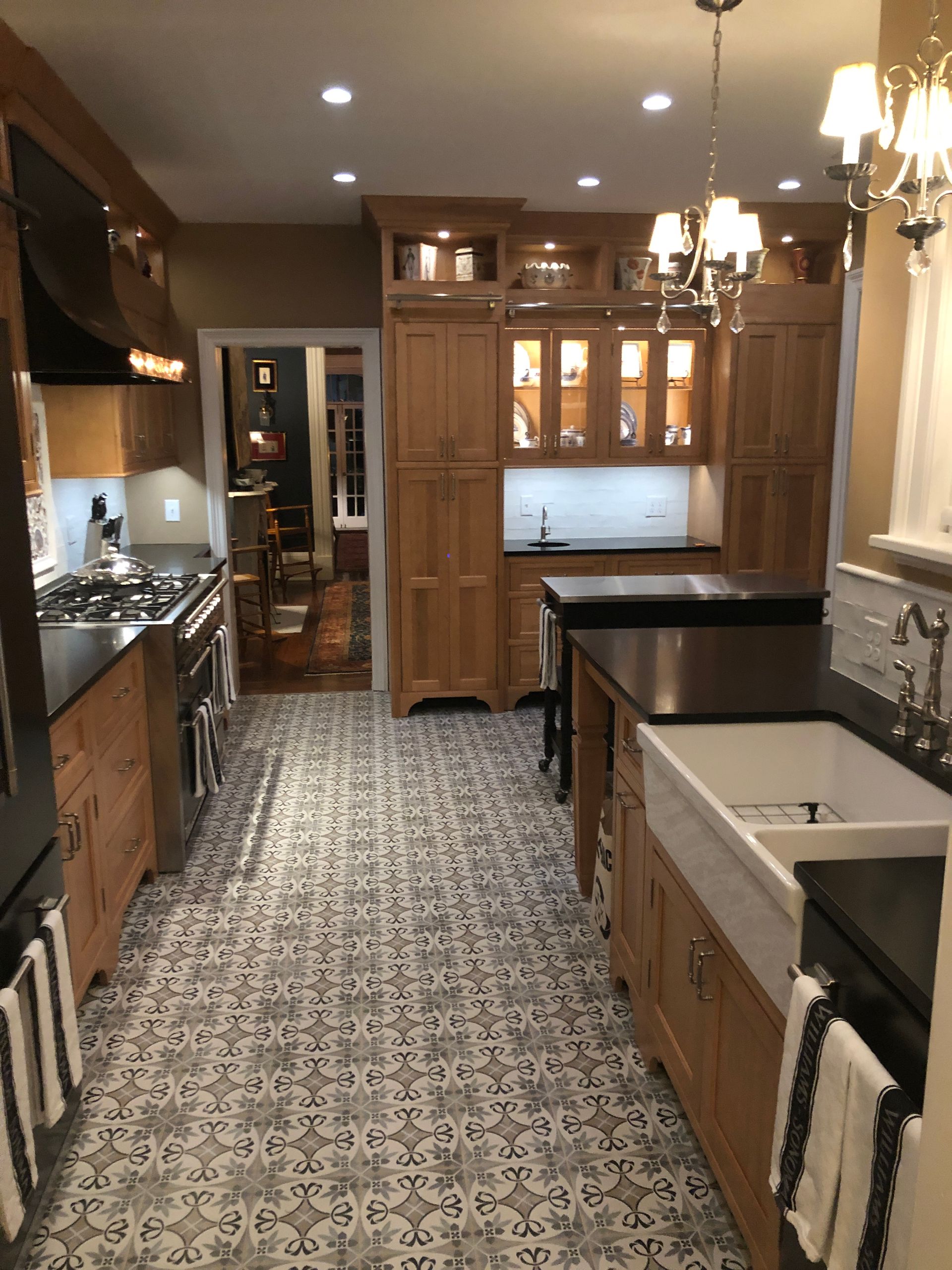 Narrow kitchen with wood cabinets, black countertops, patterned floor, and a white island sink