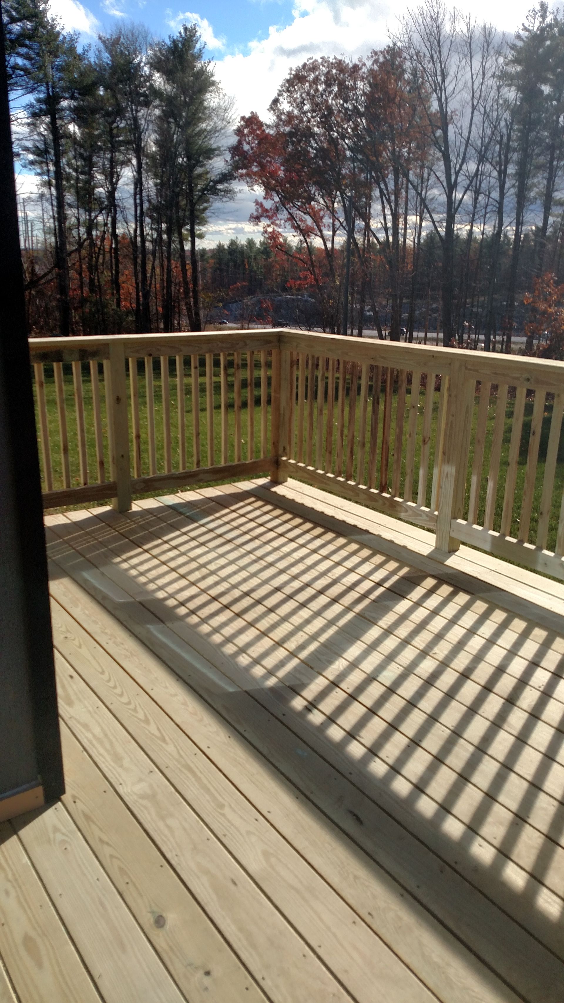 Sunlit wooden deck with railing, casting striped shadows, overlooking trees in the distance