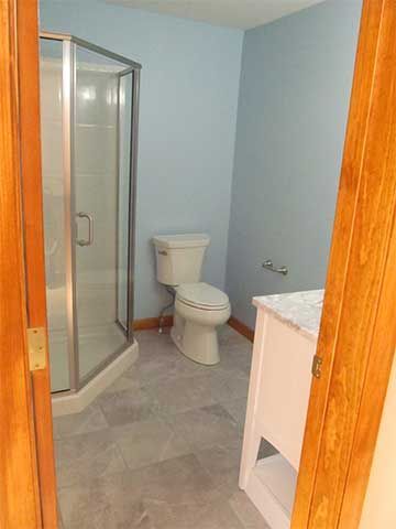 Small bathroom with shower, toilet, and sink in light blue and wood trim.