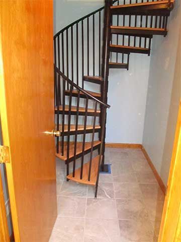 Indoor spiral staircase with dark wood steps and black railing in a tiled hallway