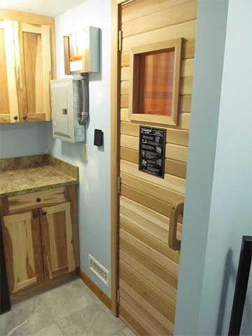 Small wood-paneled sauna room with a glass door and stone bench inside