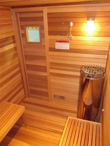 Wood-paneled sauna with benches, heater, and wall lamp lit warmly.