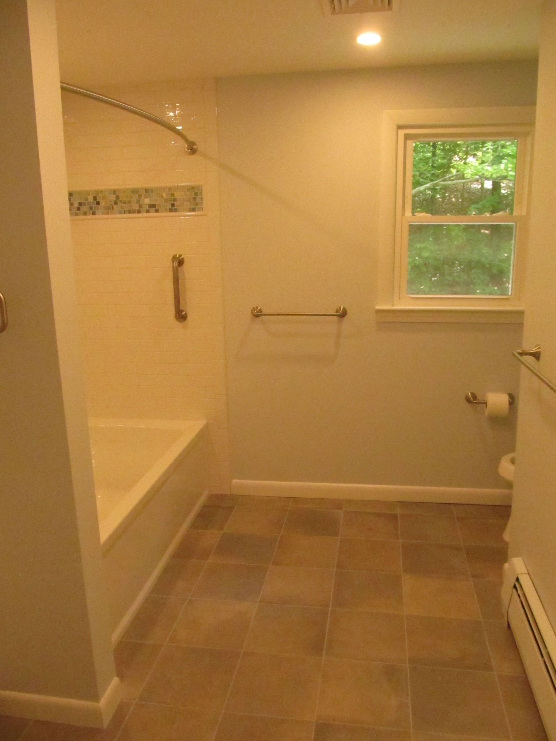 Accessible bathroom with walk-in tub, grab bars, tiled floor, and window.