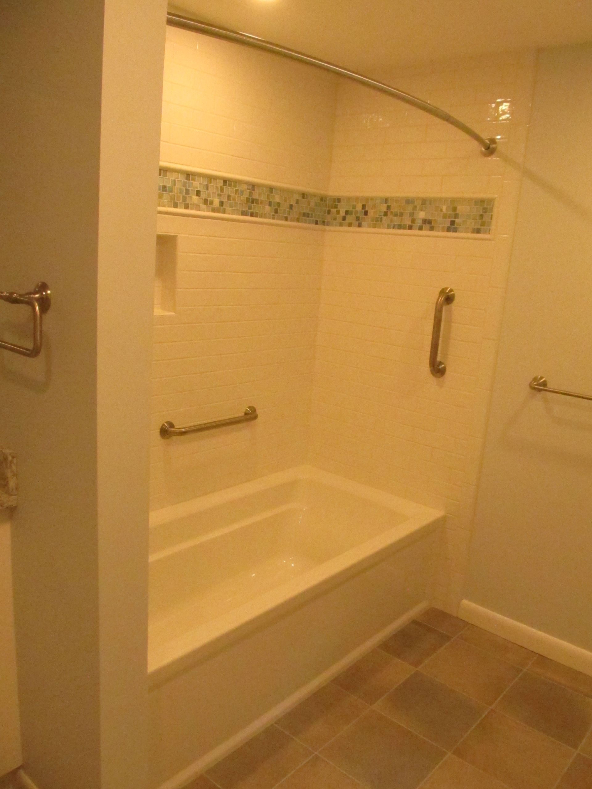 Bathroom with a white tub, beige tile, grab bars, and a shower curtain rod.