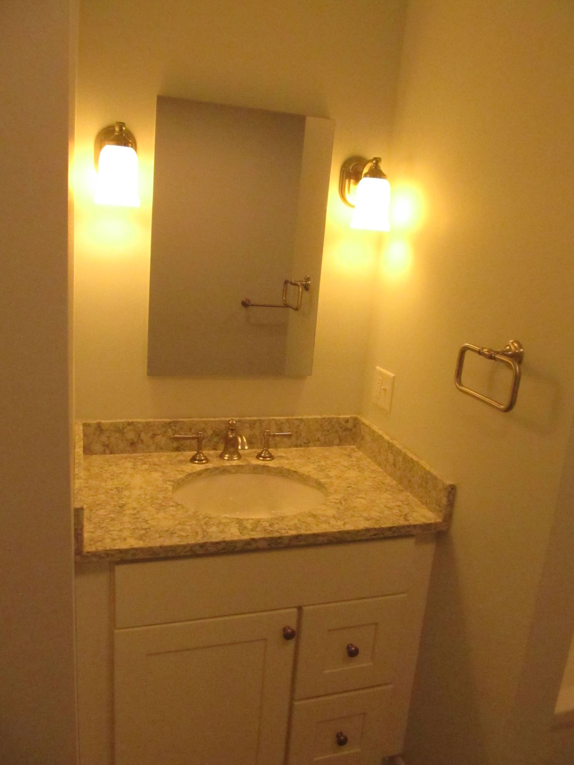 Small bathroom vanity with granite sink, mirror, and wall lights in a beige room.