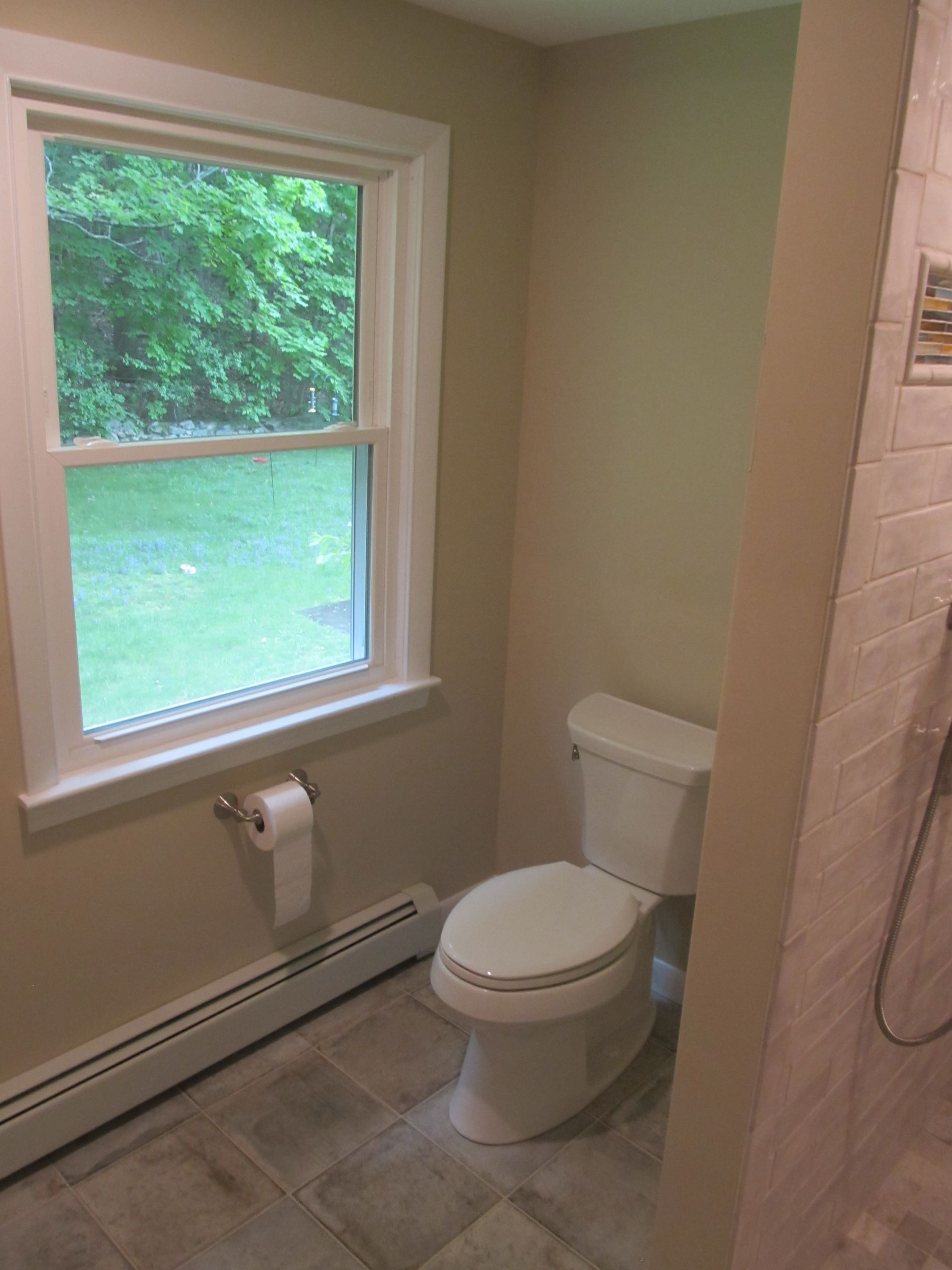 Small beige bathroom with a toilet, window, and wall-mounted toilet paper holder.