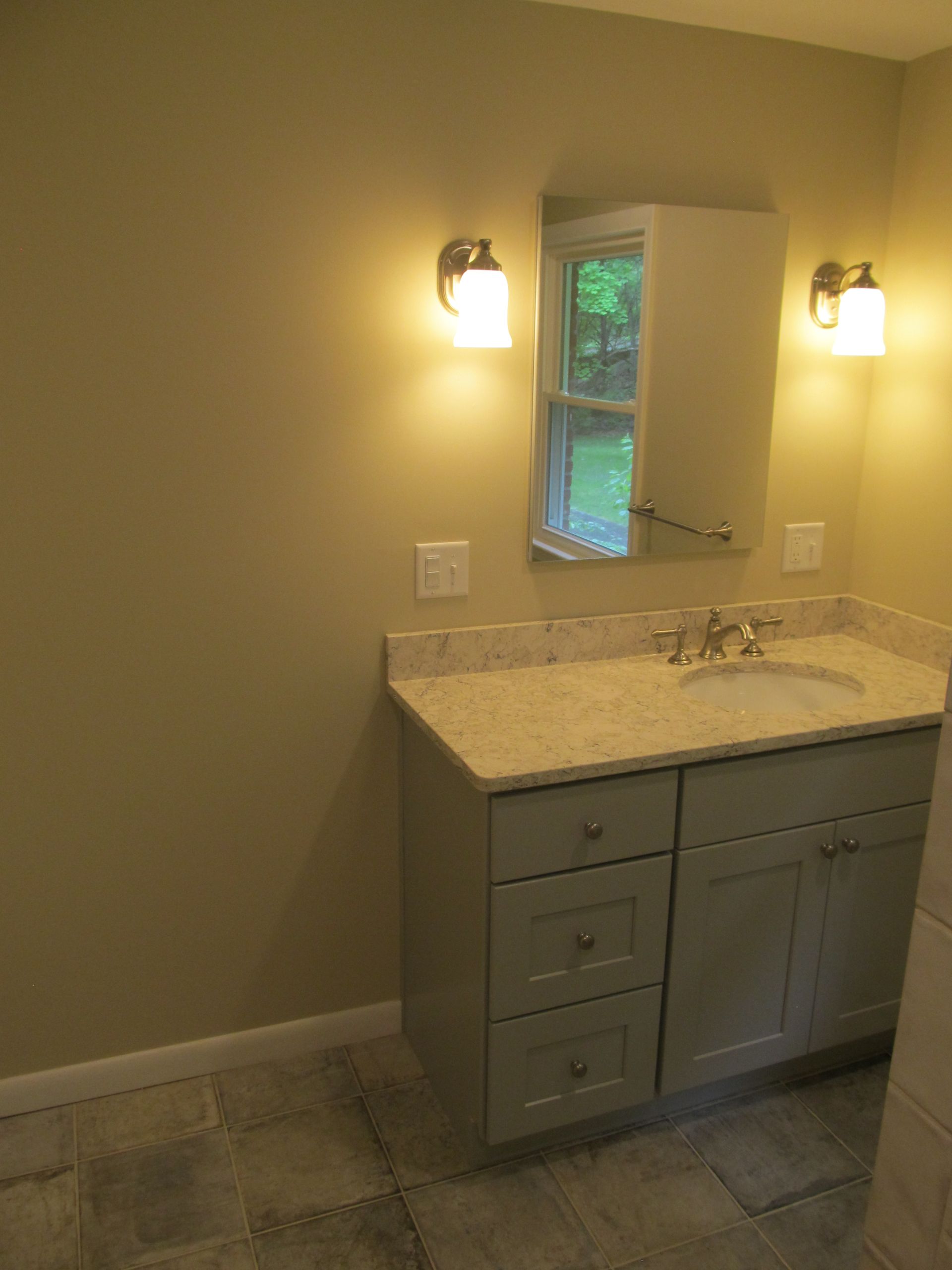 Small bathroom vanity with granite countertop, wall mirror, and two lit sconces in beige room